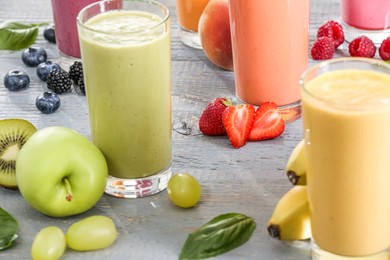 Photo of Many different delicious smoothies and ingredients on grey wooden table, closeup