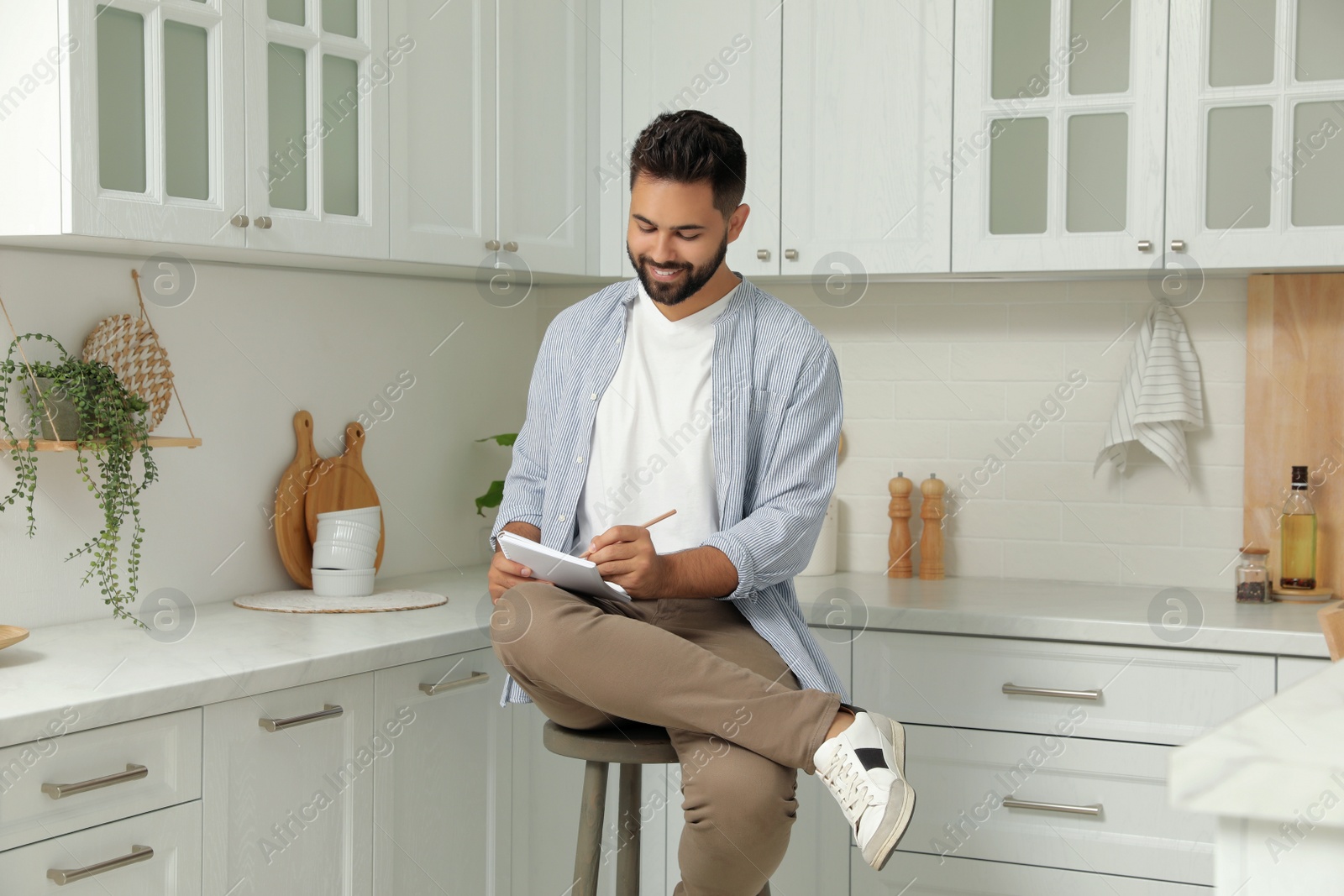 Photo of Handsome young man with notebook sitting on stool in kitchen