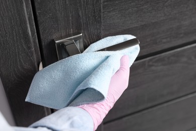 Woman wiping door handle with rag indoors, closeup