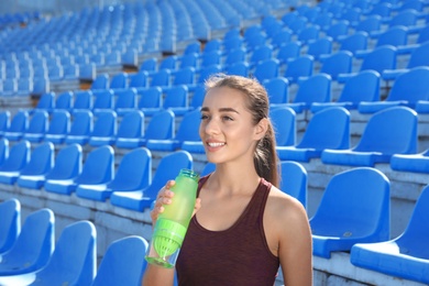 Photo of Young sporty woman holding bottle of water at stadium on sunny day