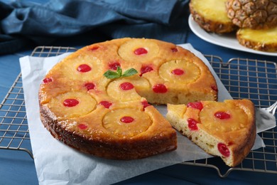 Photo of Delicious cut pineapple pie with cherry on blue table, closeup