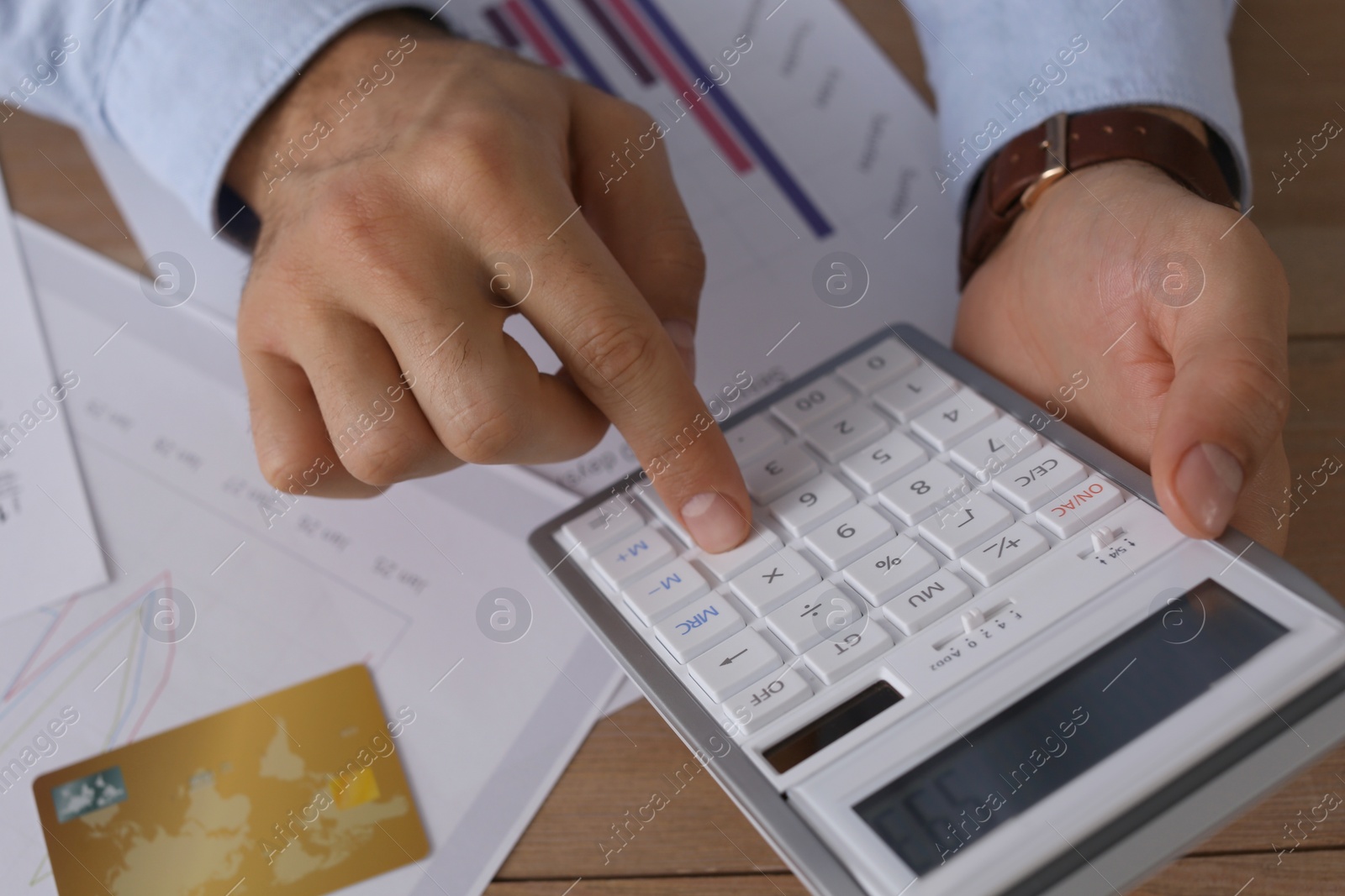 Photo of Tax accountant with calculator working at wooden table, closeup