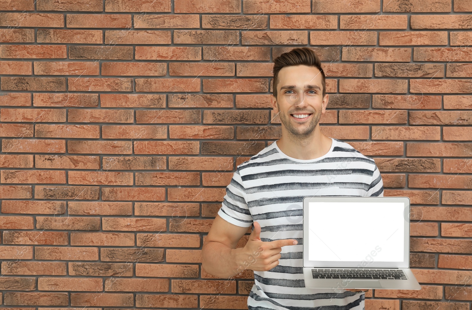 Photo of Man in casual clothes with laptop near brick wall