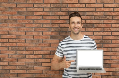 Man in casual clothes with laptop near brick wall