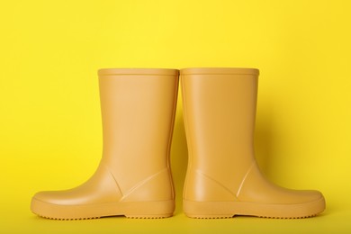 Photo of Pair of bright rubber boots on yellow background
