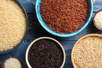 Flat lay composition with brown and other types of rice in bowls on color wooden background