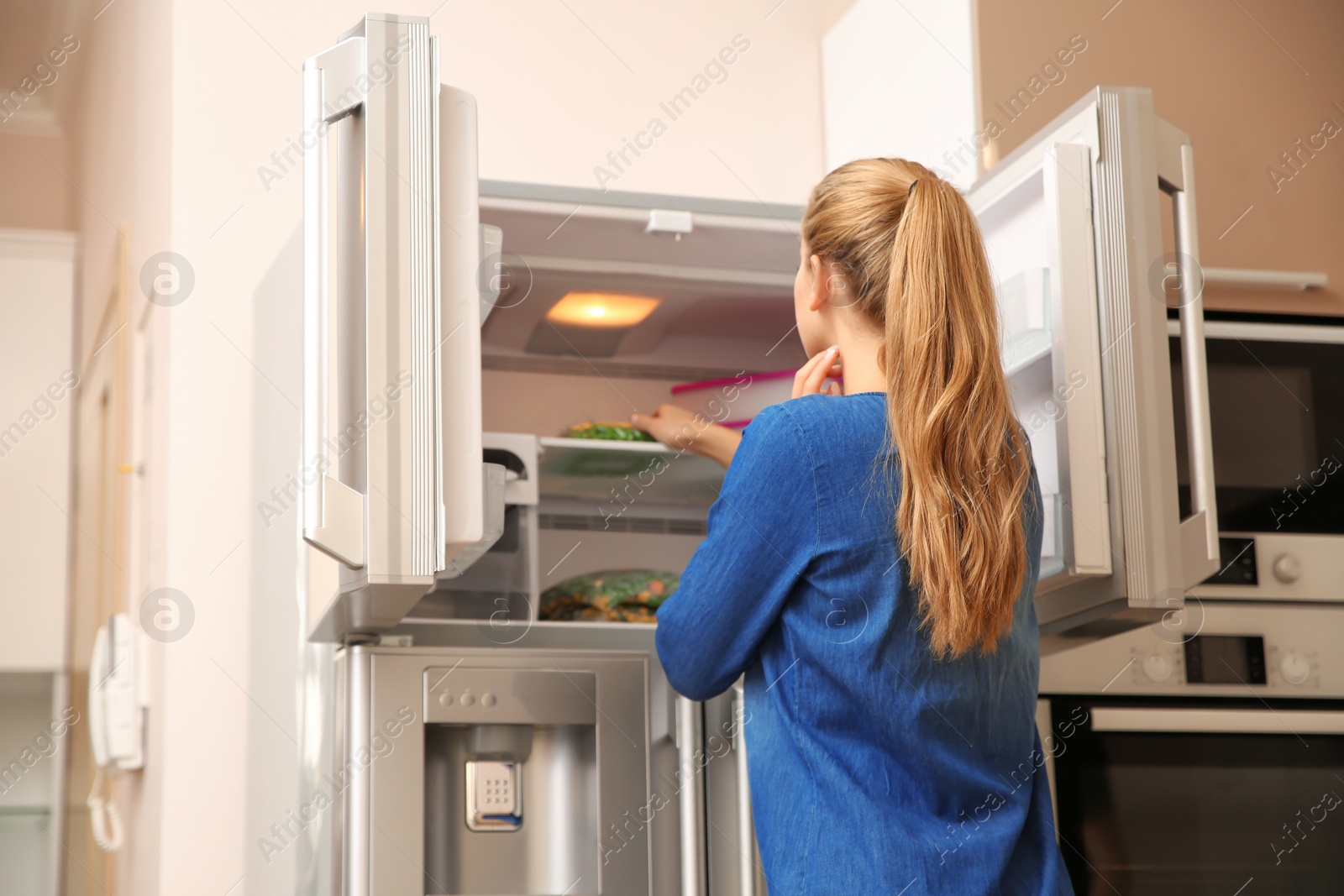 Photo of Young woman choosing food in refrigerator at home