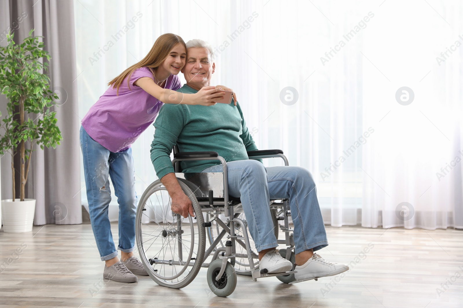 Photo of Teenage girl with grandfather in wheelchair taking selfie at home