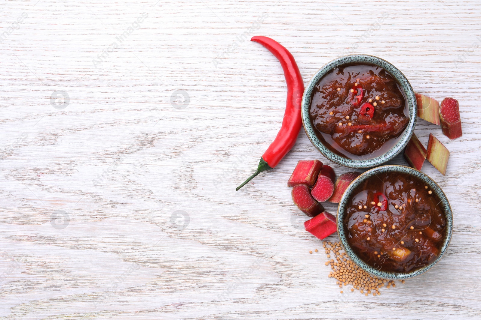 Photo of Tasty rhubarb sauce and ingredients on white wooden table, flat lay. Space for text