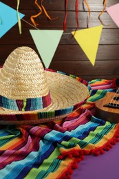 Mexican sombrero hat, ukulele and poncho on purple table, closeup