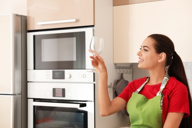 Photo of Young woman holding clean glass in kitchen. Dish washing