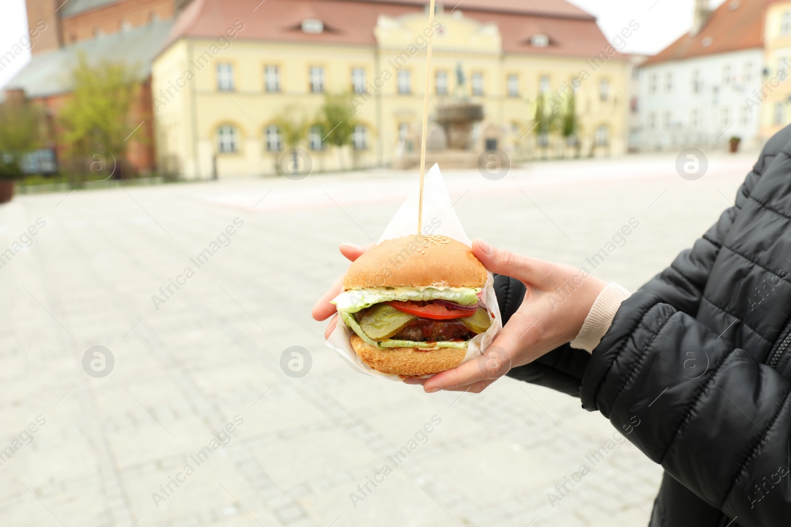 Photo of Closeup of woman holding fresh delicious burger outdoors, space for text. Street food
