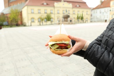 Closeup of woman holding fresh delicious burger outdoors, space for text. Street food