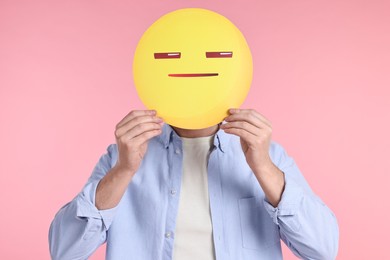 Photo of Man holding emoticon with closed eyes and mouth on pink background