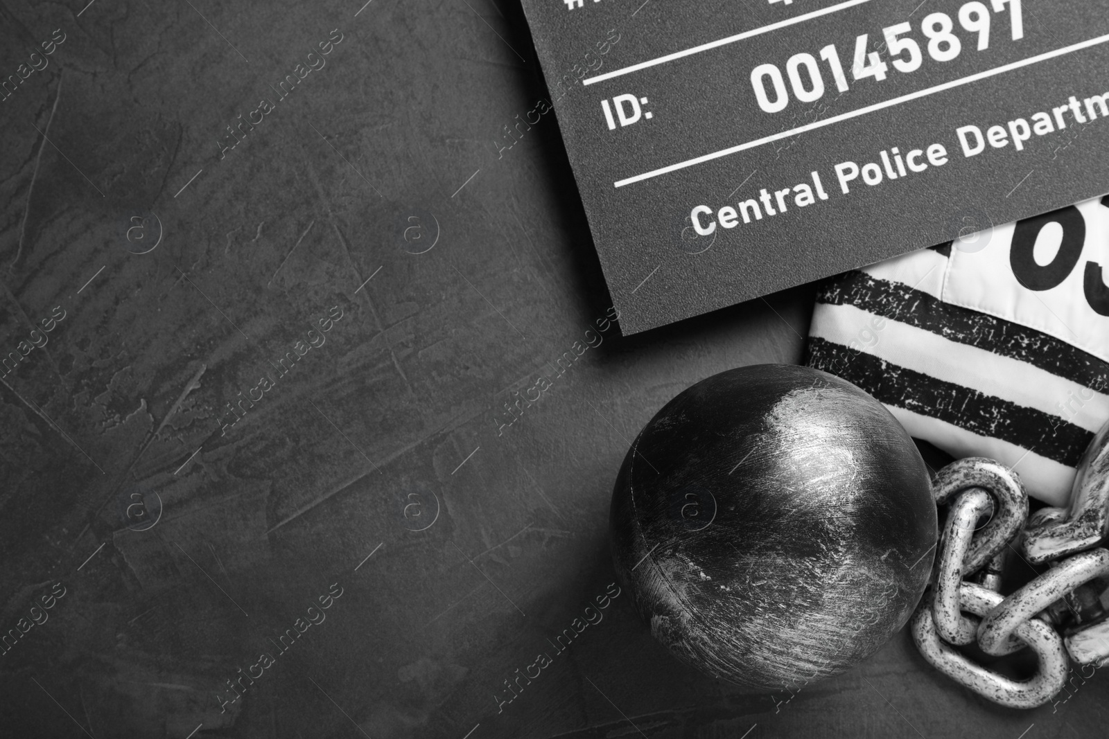 Photo of Metal ball with chain, prison uniform and mugshot letter board on grey table, flat lay. Space for text