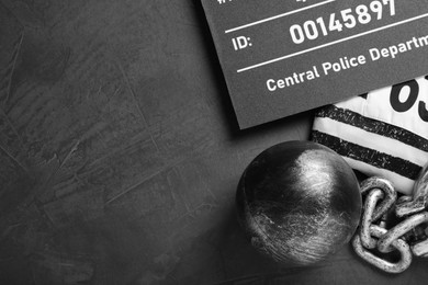 Photo of Metal ball with chain, prison uniform and mugshot letter board on grey table, flat lay. Space for text