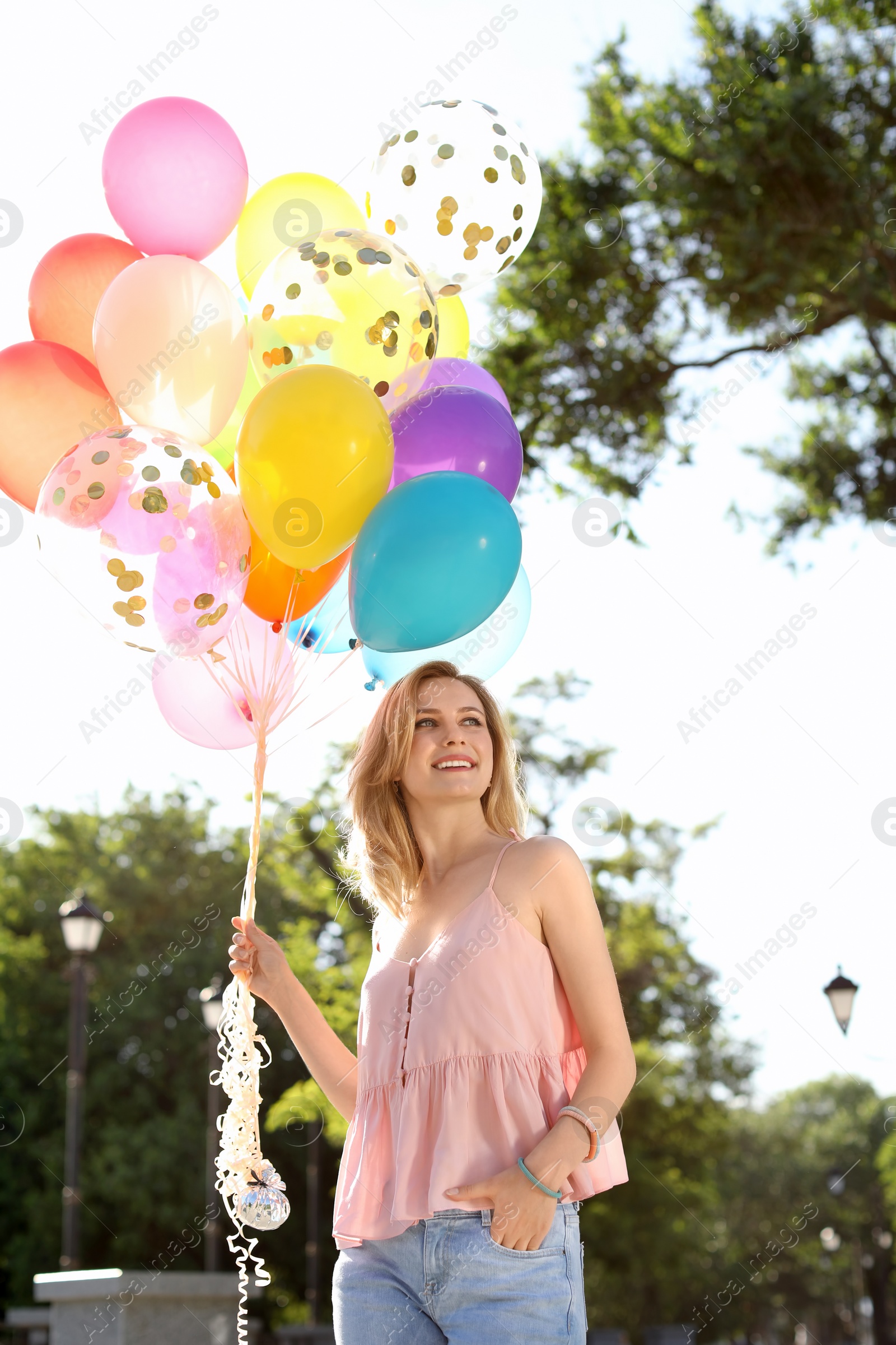 Photo of Young woman with colorful balloons outdoors on sunny day