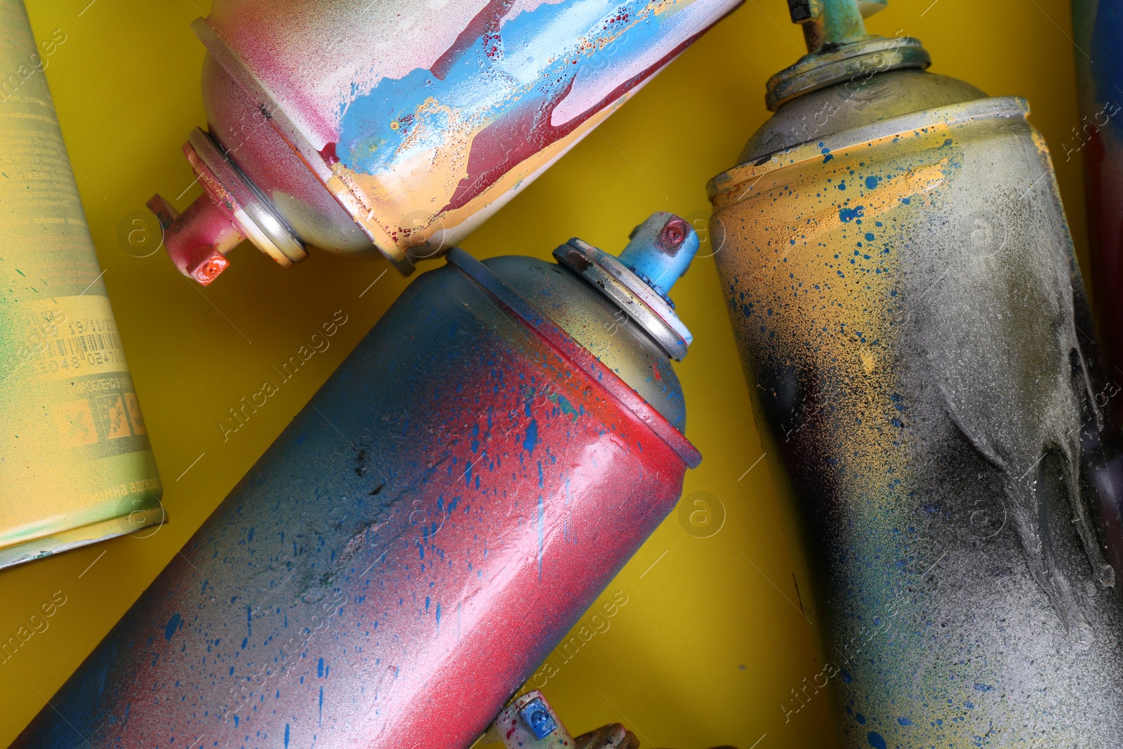 Photo of Many spray paint cans on yellow background, flat lay