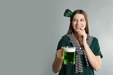 Photo of Happy woman in St Patrick's Day outfit with beer on light grey background, space for text