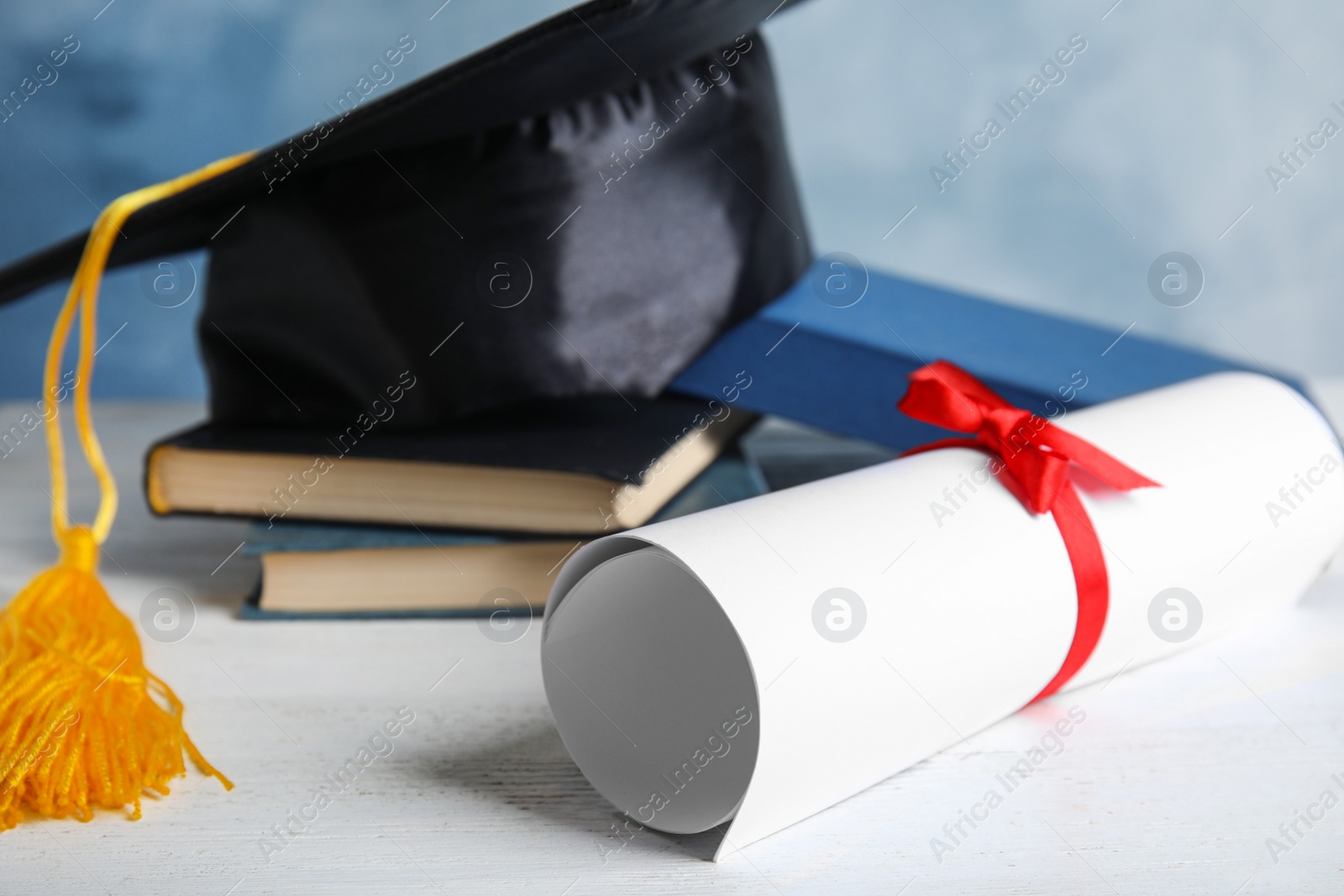 Photo of Graduation hat, books and student's diploma on white wooden table against light blue background, closeup