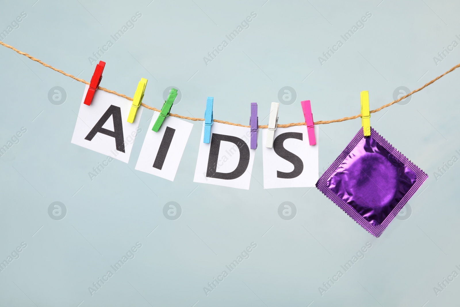 Photo of Paper sheets with word AIDS and violet condom hanging on clothesline against light grey background. Safe sex