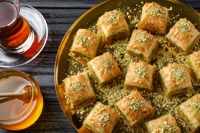 Photo of Delicious fresh baklava with chopped nuts served on black wooden table, flat lay. Eastern sweets