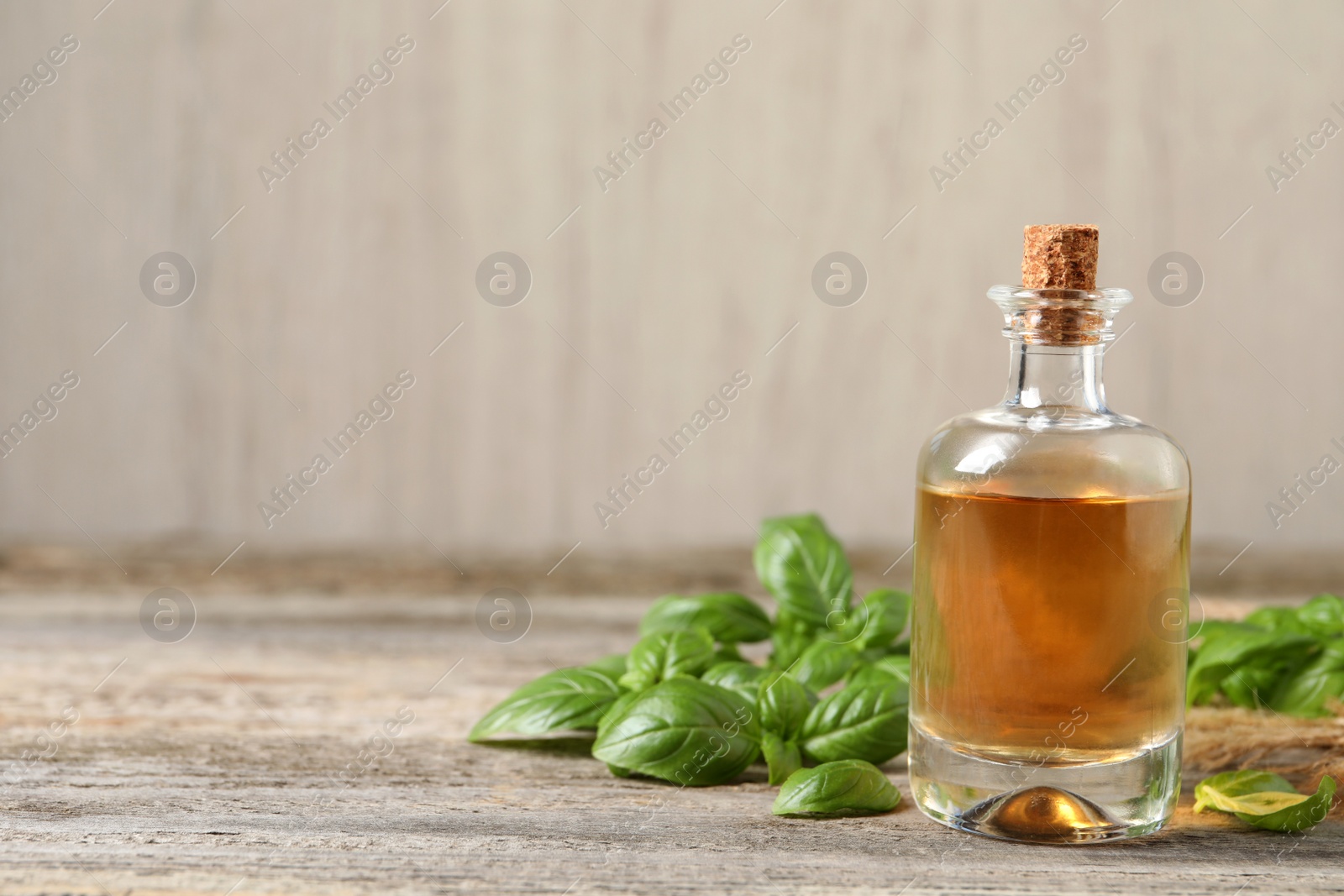 Photo of Glass bottle of basil essential oil and leaves on wooden table. Space for text