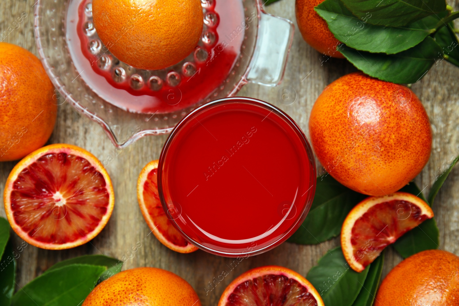 Photo of Tasty sicilian orange juice in glass, squeezer and fruits on wooden table, flat lay