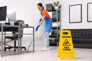 Photo of Cleaning service worker washing floor with mop in office, focus on wet floor sign