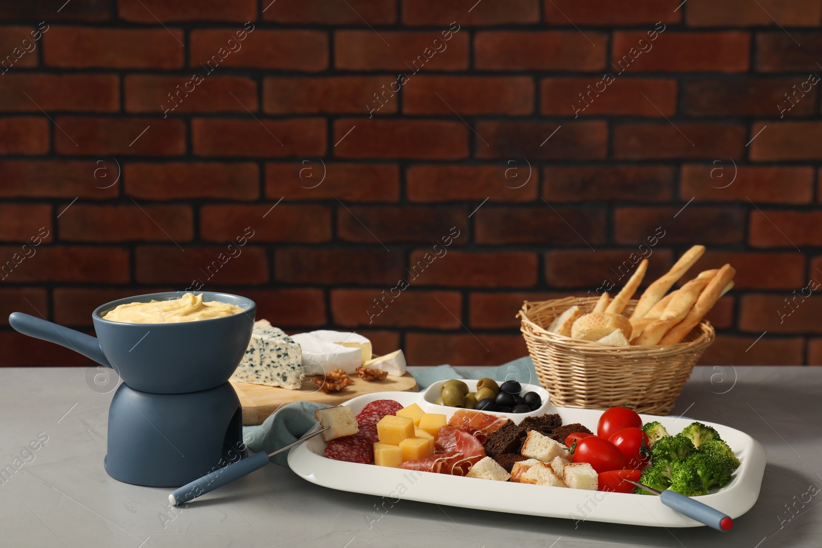 Photo of Fondue with tasty melted cheese, forks and different snacks on grey table