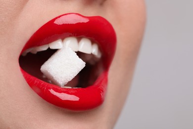 Closeup view of young woman with beautiful lips eating sugar cube on light grey background