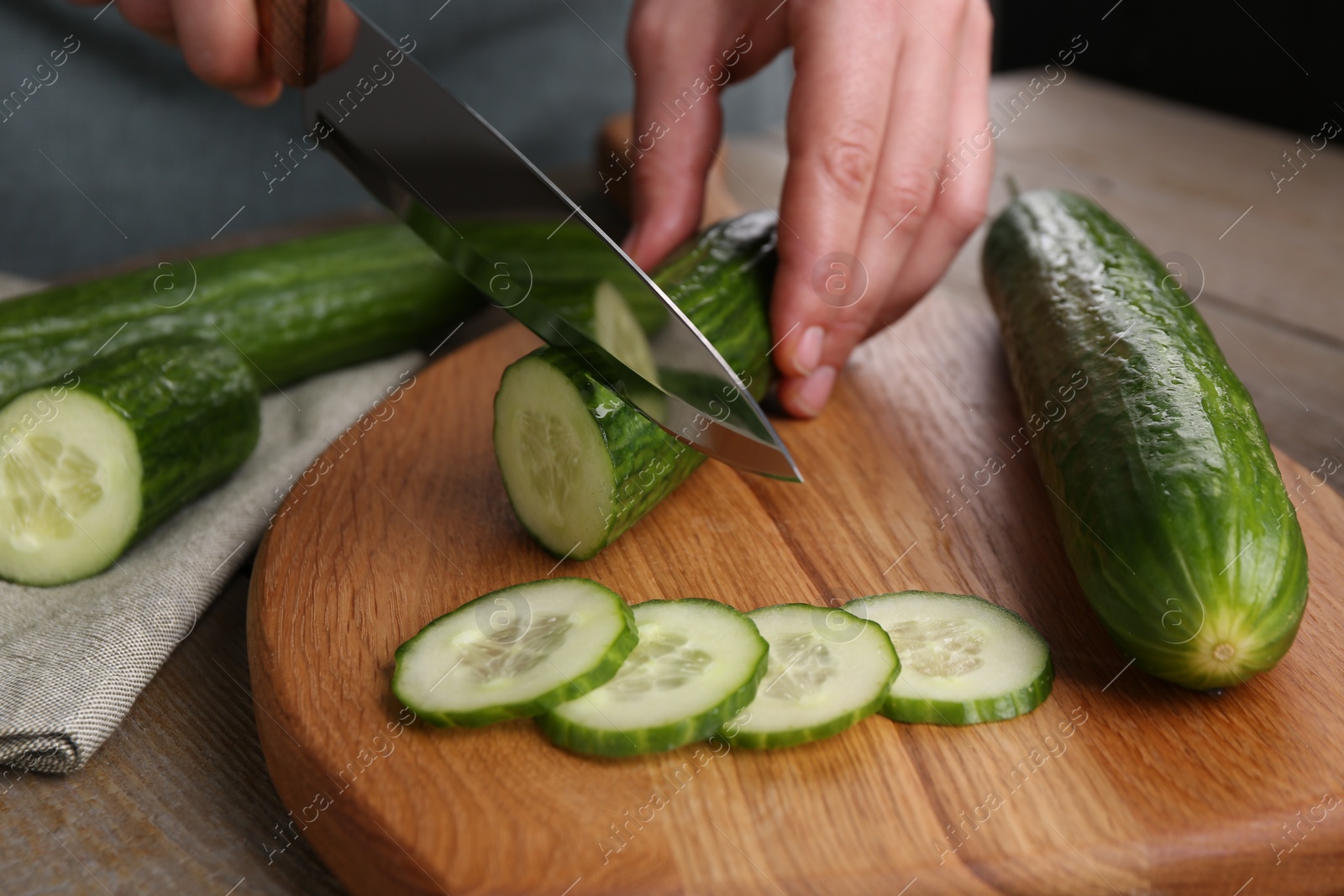 Photo of Woman cutting cucumber on wooden board at table, closeup