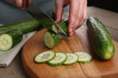 Woman cutting cucumber on wooden board at table, closeup