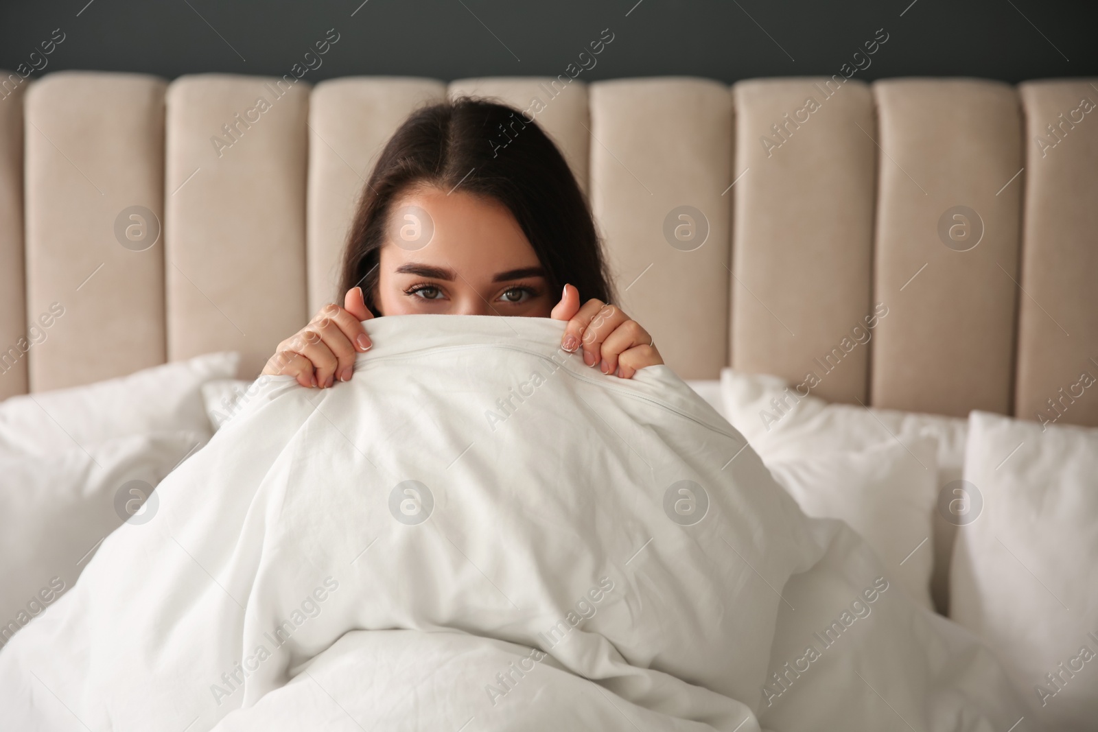 Photo of Beautiful young woman wrapped with soft blanket relaxing on bed at home