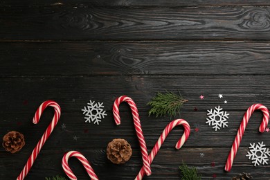 Flat lay composition with candy canes and Christmas decor on black wooden table. Space for text