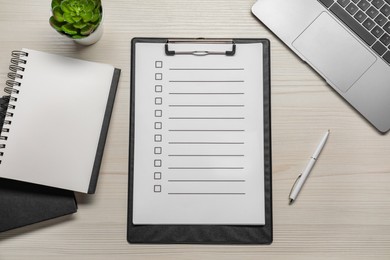 Clipboard with checkboxes, pen and laptop on wooden table, flat lay