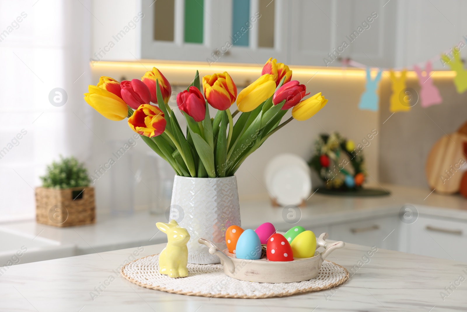 Photo of Easter decorations. Bouquet of tulips, painted eggs and bunny figure on table indoors