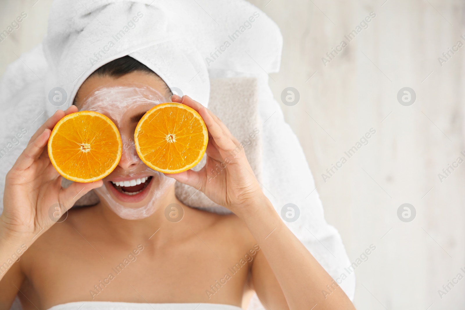 Photo of Pretty woman with rejuvenating facial mask holding sliced orange in spa salon, above view