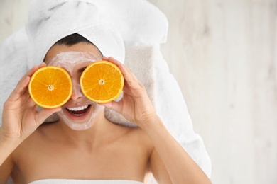 Photo of Pretty woman with rejuvenating facial mask holding sliced orange in spa salon, above view