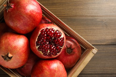 Photo of Ripe pomegranates in crate on wooden table, top view