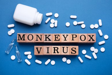 Photo of Words Monkeypox Virus made of wooden cubes, vials and pills on blue background, flat lay