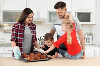 Photo of Happy family with tray of oven baked buns in kitchen