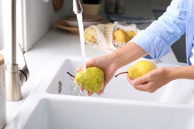 Photo of Woman washing fresh ripe pears in kitchen, closeup