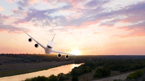 Modern airplane flying in sky during sunset