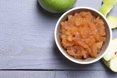 Photo of Delicious apple jam in bowl and fresh fruits on grey wooden table, flat lay. Space for text