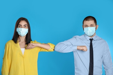 Photo of Man and woman bumping elbows to say hello on light blue background. Keeping social distance during coronavirus pandemic