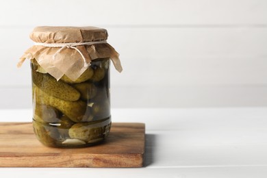 Photo of Tasty pickled cucumbers in jar on white table. Space for text