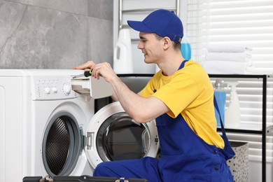 Photo of Smiling plumber with screwdriver repairing washing machine in bathroom