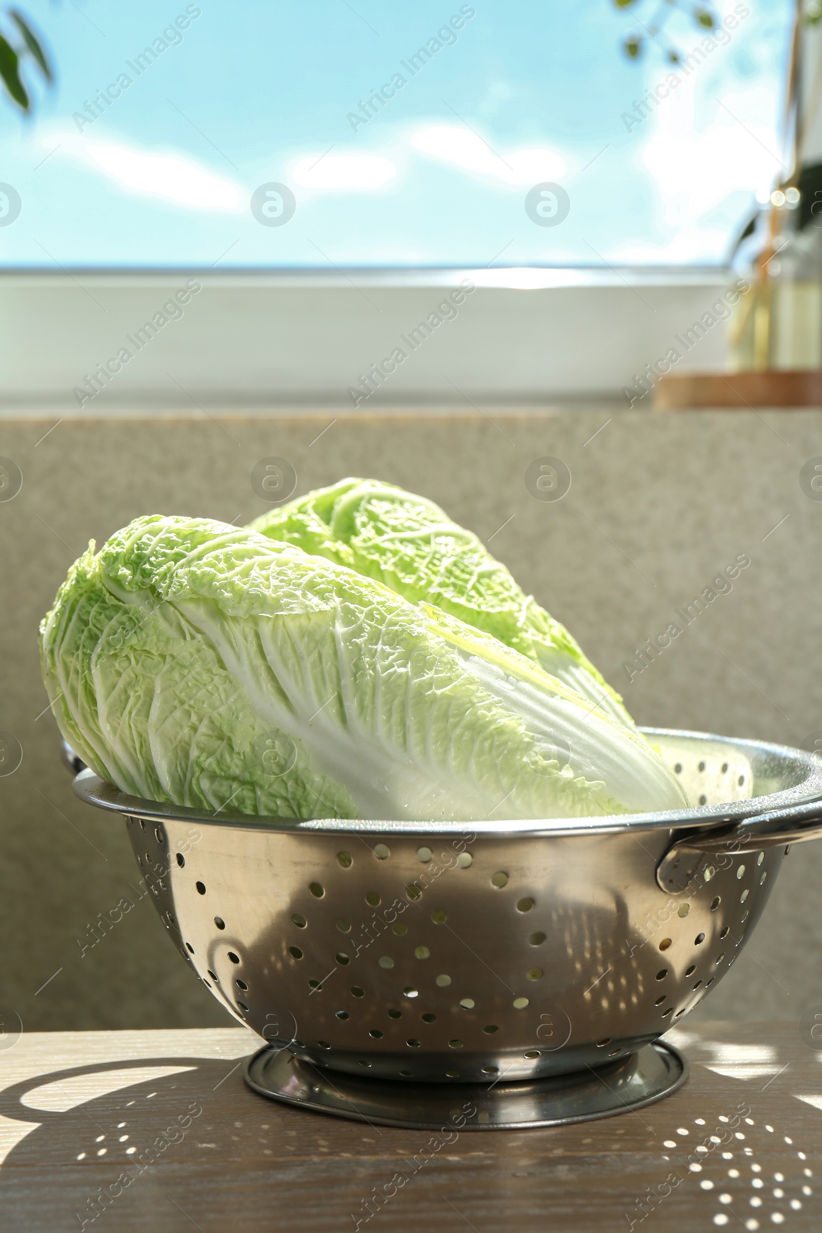 Photo of Fresh Chinese cabbages in colander on light wooden table indoors