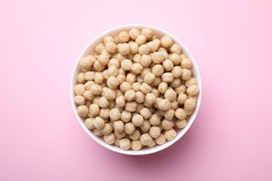 Photo of Tasty cereal balls in bowl on pink table, top view